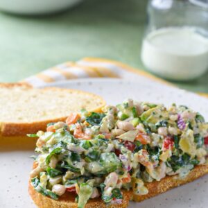 A mediterranean chopped sandwich on a white plate with homemade ranch dressing behind it