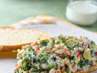 A mediterranean chopped sandwich on a white plate with homemade ranch dressing behind it