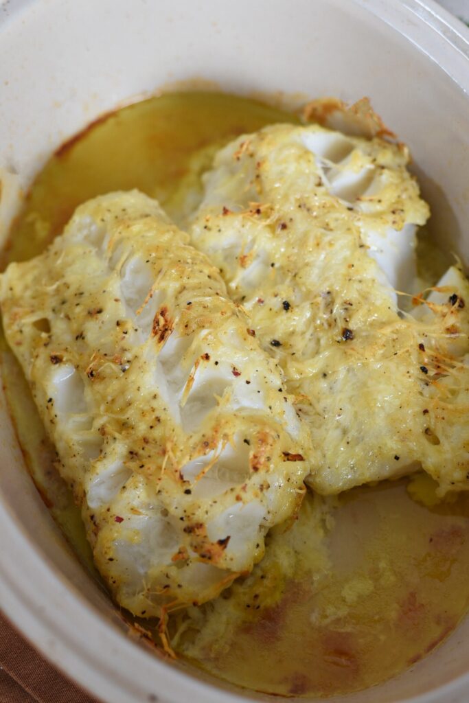 Baked parmesan crusted cod in a baking dish with a golden crispy cheese topper