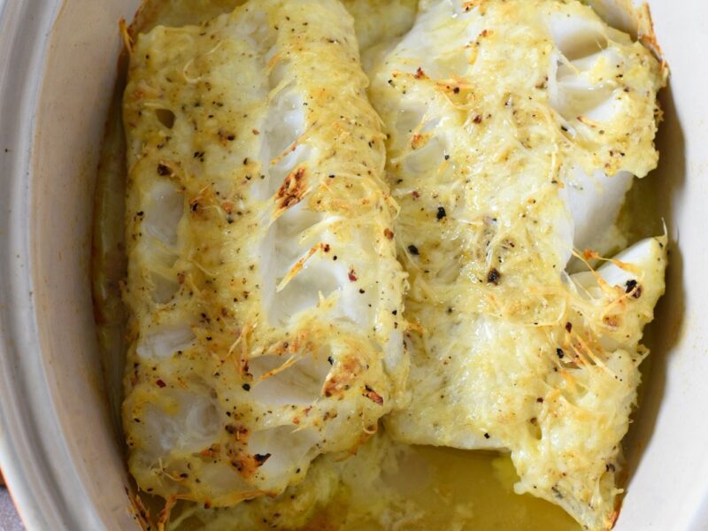 An overhead shot of baked parmesan crusted cod in a baking dish surrounded by liquid