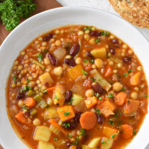 Sardinian minestrone soup in a white bowl with bread next to it.