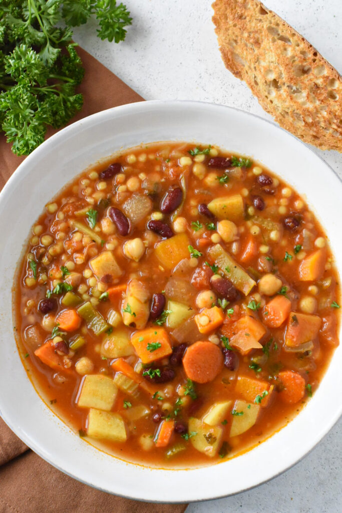 Sardinian minestrone soup in a white bowl with bread next to it.