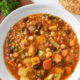 Sardinian minestrone soup in a white bowl with bread next to it.