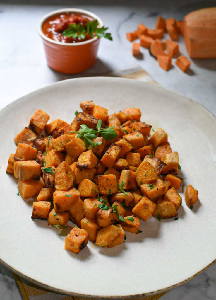 Air fryer sweet potato cubes on a white plate garnished with parsley.
