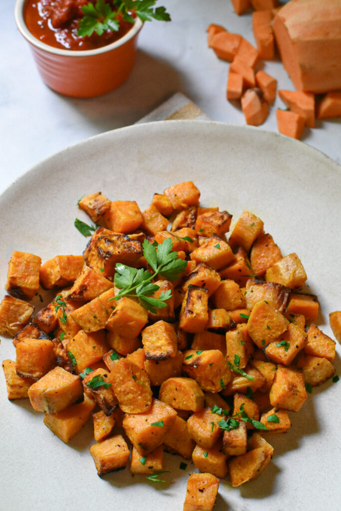 Air fried sweet potato cubes on a white plate garnished with parsley.