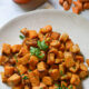 Air fried sweet potato cubes on a white plate garnished with parsley.