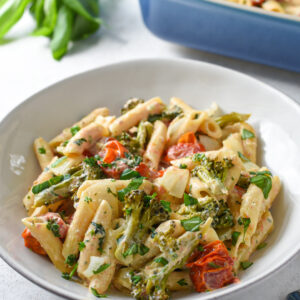 Boursin cheese pasta in a white bowl with cherry tomatoes, broccoli and basil on top.