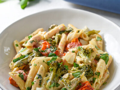 Boursin cheese pasta in a white bowl with cherry tomatoes, broccoli and basil on top.