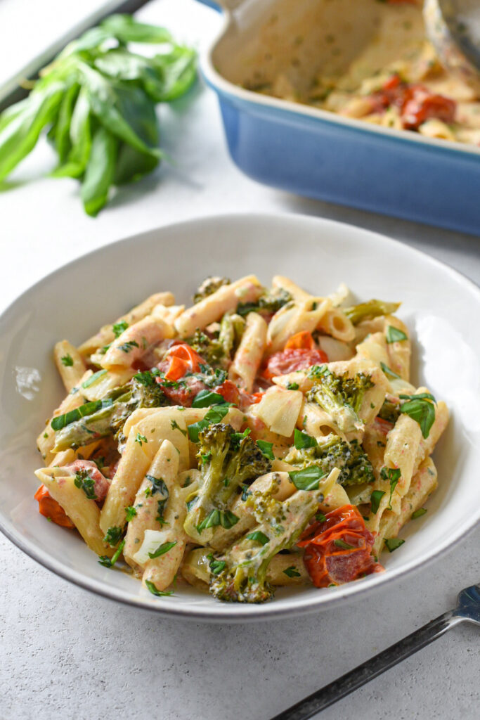 Boursin cheese pasta in a white bowl with cherry tomatoes, broccoli and basil on top.