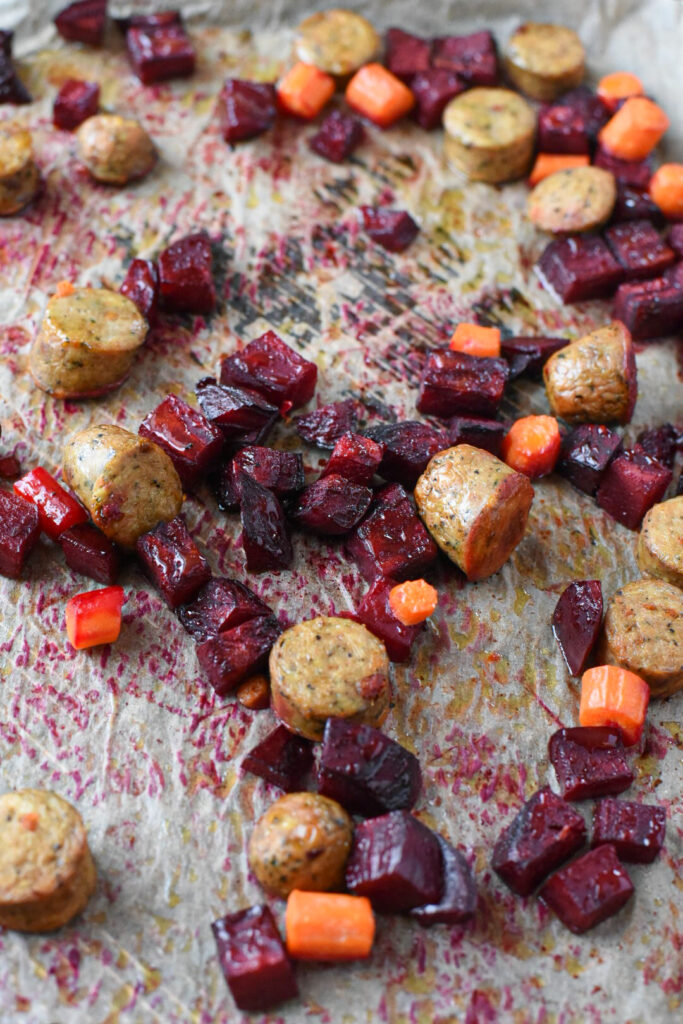 A parchment paper lined baking sheet with roasted beets, carrots and sausage.
