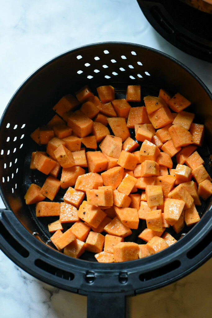 cubed sweet potatoes in air fryer Raw cubed sweet potato in air fryer basket.