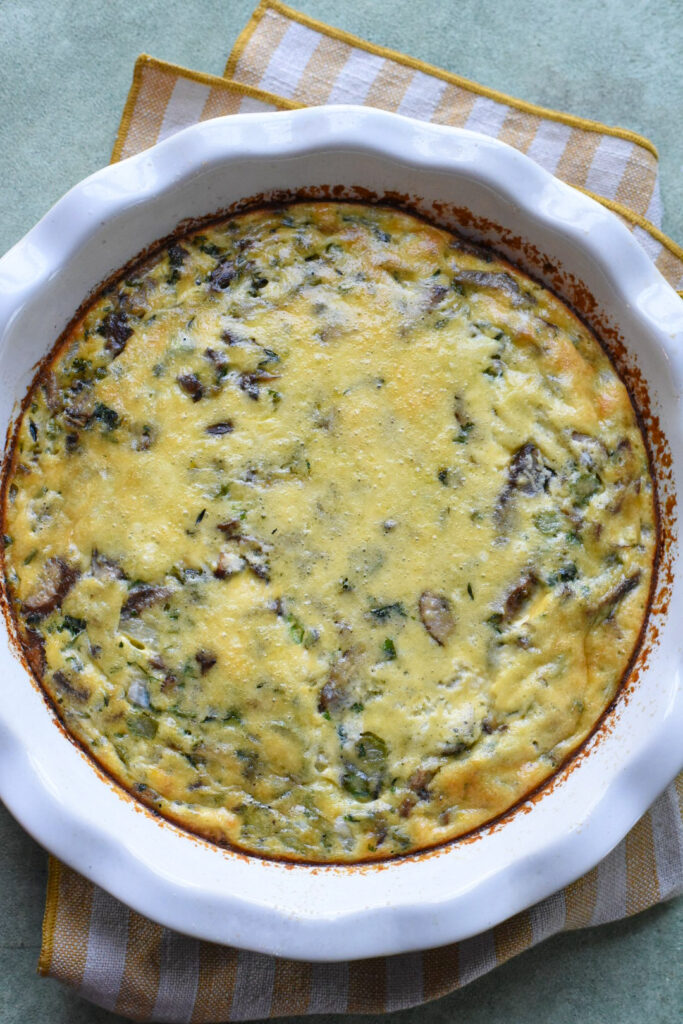 A baked frittata with veggies in a white pie dish.