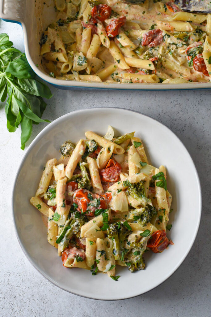 A healthy boursin cheese pasta recipe in a white bowl with a baking dish filled with pasta above it.