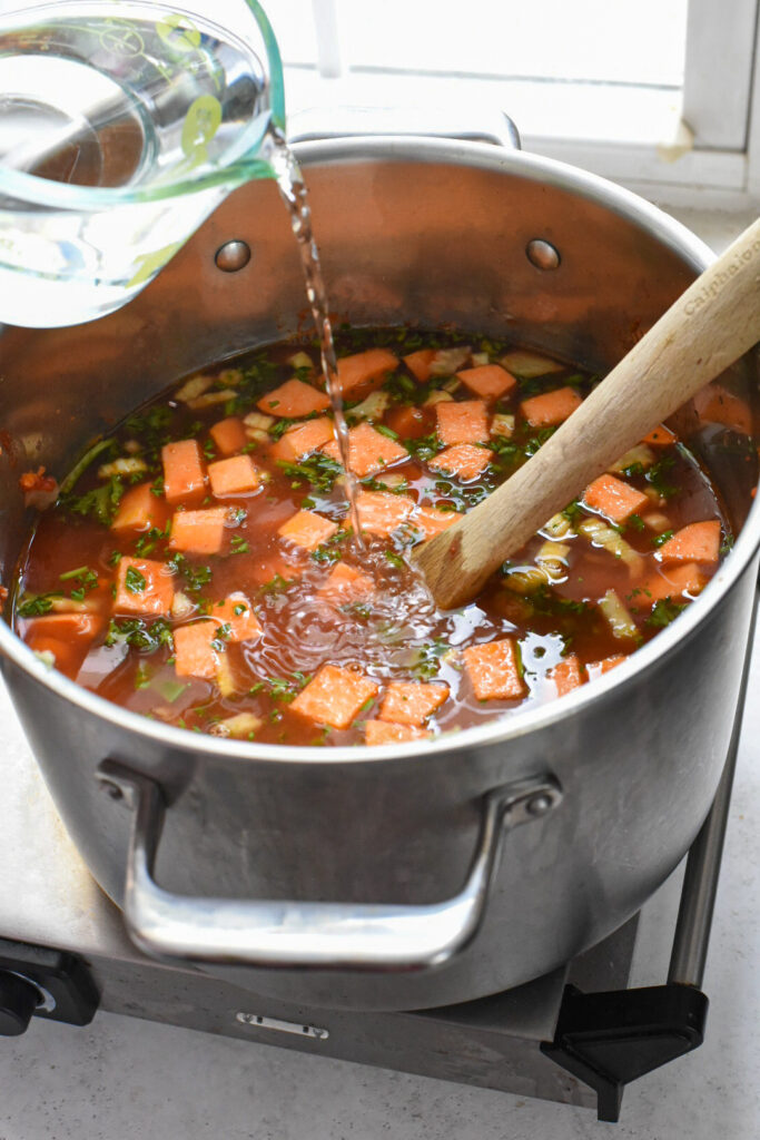 minestrone soup with water Water pouring into a soup in a stock pot.