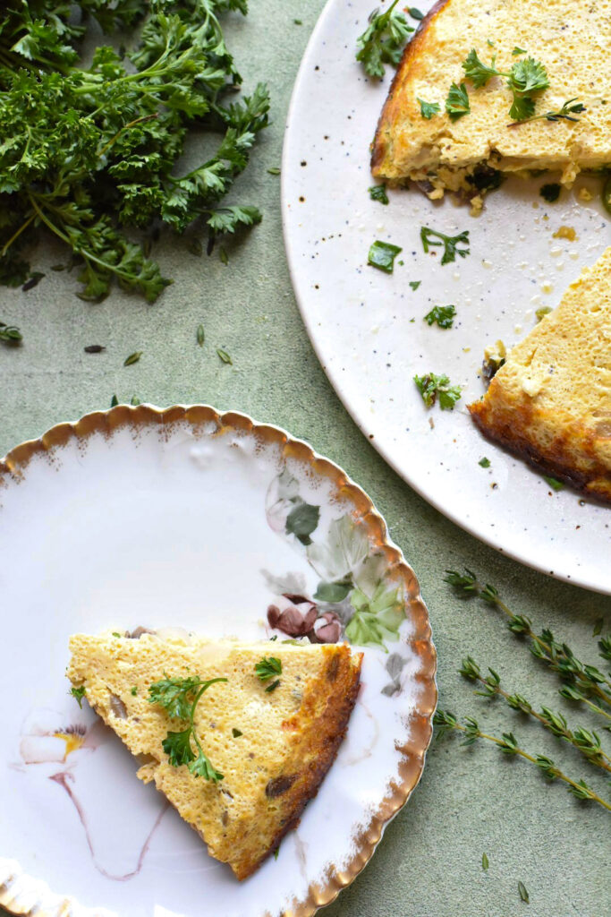 A slice of vegetable frittata on a plate next to a baked frittata