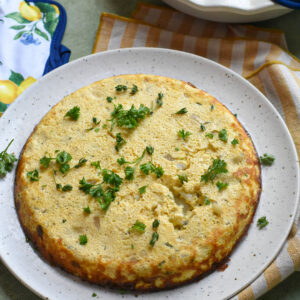 An egg and vegetable frittata on a plate garnished with fresh herbs.
