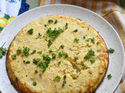 An egg and vegetable frittata on a plate garnished with fresh herbs.