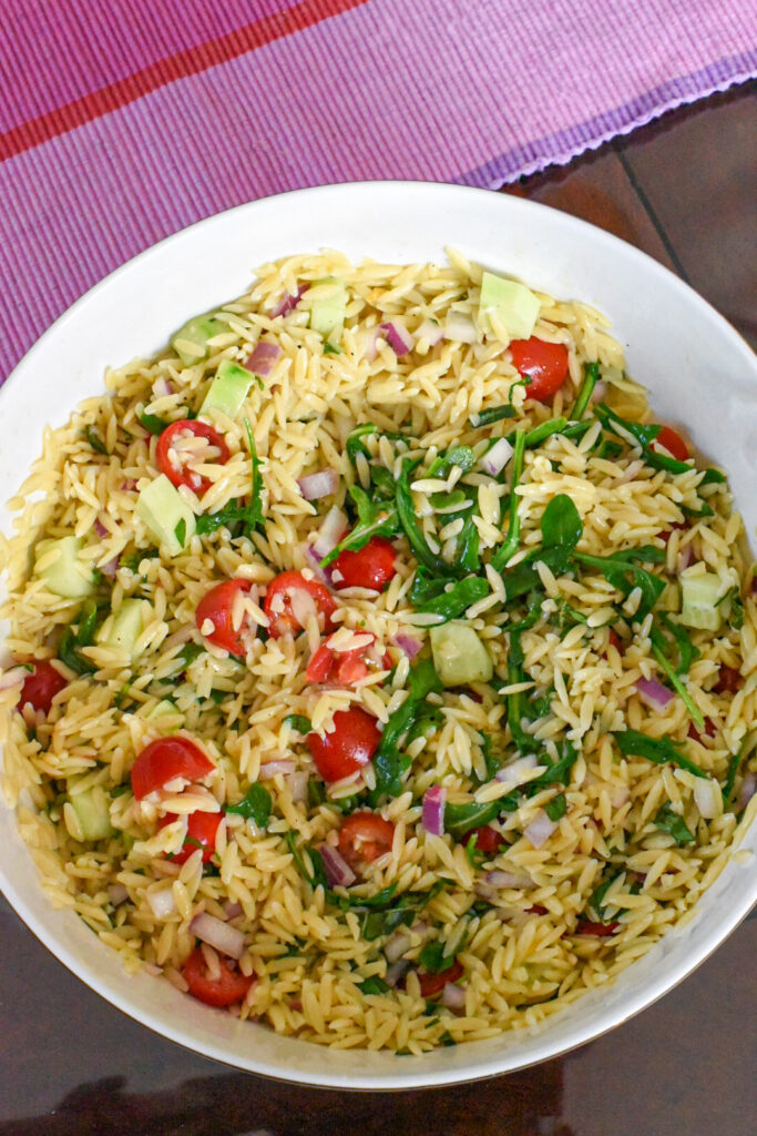 quick orzo pasta salad recipe A large serving bowl filled with orzo salad with tomatoes, red onion, arugula, and cucumber.