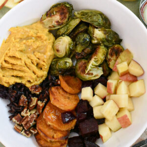 A fall harvest bowl filled with apple, brussels sprouts, sweet potato, pumpkin hummus, beets, wild rice and walnuts.
