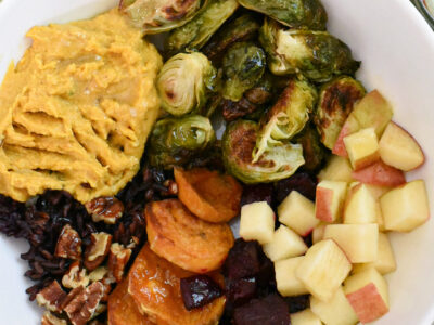 A fall harvest bowl filled with apple, brussels sprouts, sweet potato, pumpkin hummus, beets, wild rice and walnuts.