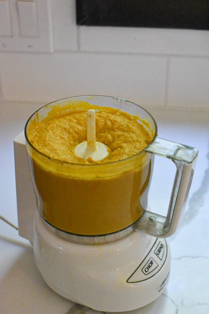 A food processor filled with bright orange processed pumpkin hummus.