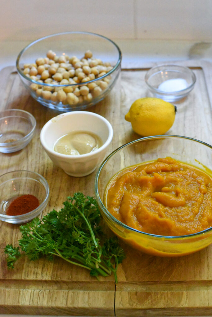 Ingredients to make hummus with pumpkin puree on a wooden cutting board.