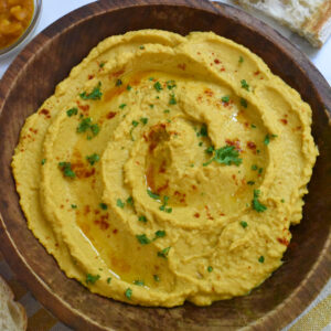 A wooden bowl filled with pumpkin hummus sprinkled with parsley and paprika.