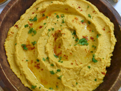 A wooden bowl filled with pumpkin hummus sprinkled with parsley and paprika.