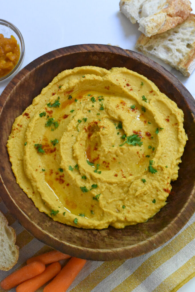 A wooden bowl filled with pumpkin hummus sprinkled with parsley and paprika.