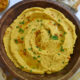 A wooden bowl filled with pumpkin hummus sprinkled with parsley and paprika.