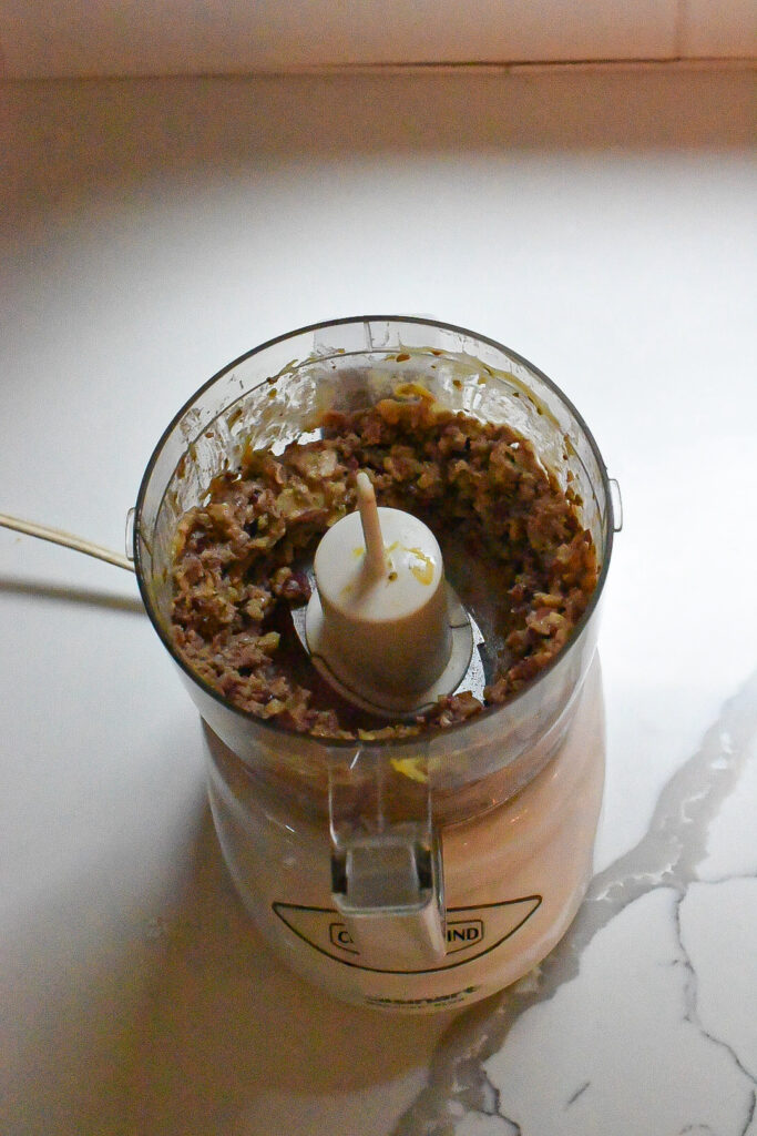 A food processor filled with processed olives and walnuts for walnut crusted salmon.