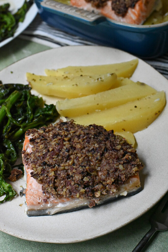 A plate filled with greek potato wedges, walnut crusted salmon and broccoli rabe.