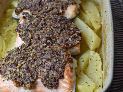 Three pieces of baked walnut crusted salmon over greek potatoes in a blue baking dish.
