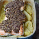Three pieces of baked walnut crusted salmon over greek potatoes in a blue baking dish.
