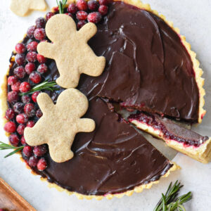 An overhead image of a chocolate cranberry tart decorated with sugary cranberries and gingerbread men.