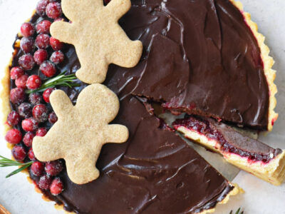 An overhead image of a chocolate cranberry tart decorated with sugary cranberries and gingerbread men.