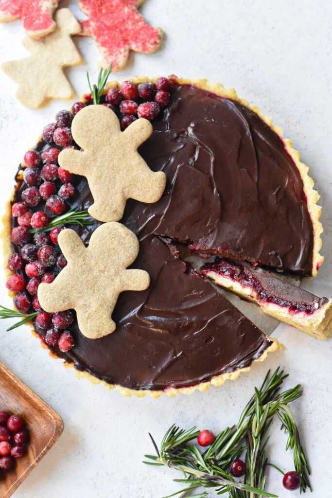 A chocolate cranberry tart decorated with sugary cranberries, rosemary and gingerbread cookies.