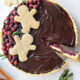 An overhead image of a chocolate cranberry tart decorated with sugary cranberries and gingerbread men.