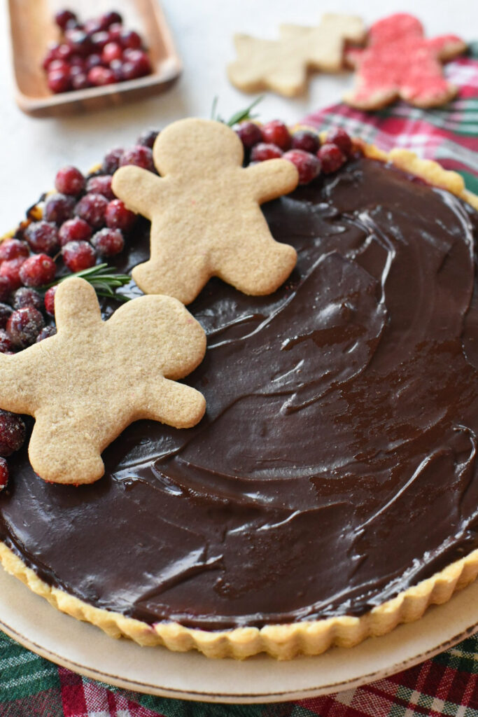 A close up image of the chocolate ganache on top of a cranberry filled tart, with gingerbread cookies on top.