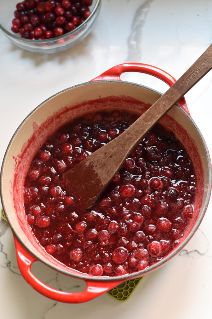 A red dutch oven filled with the making of a cranberry tart filling with whole cranberries visible.