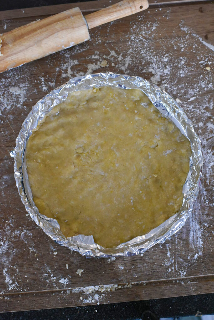 A raw tart with aluminum foil around the edged to help prevent them from burning while cooking.