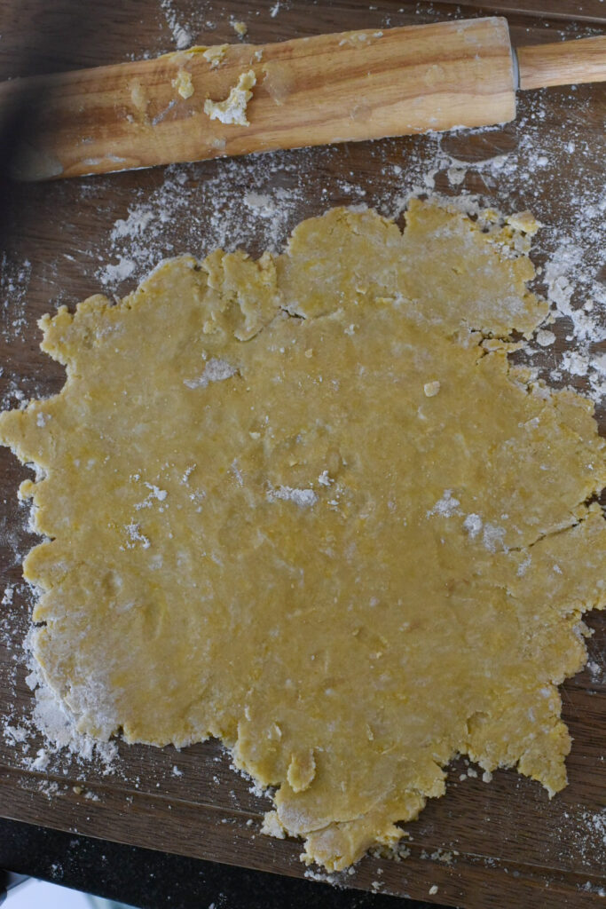 Tart dough rolled out flat onto a wooden cutting board.