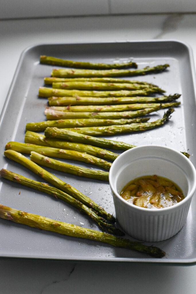 Asparagus on a baking sheet with garlic confit.