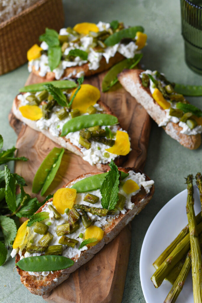 Asparagus and burrata toast on a wooden serving platter topped with peas and yellow radish.